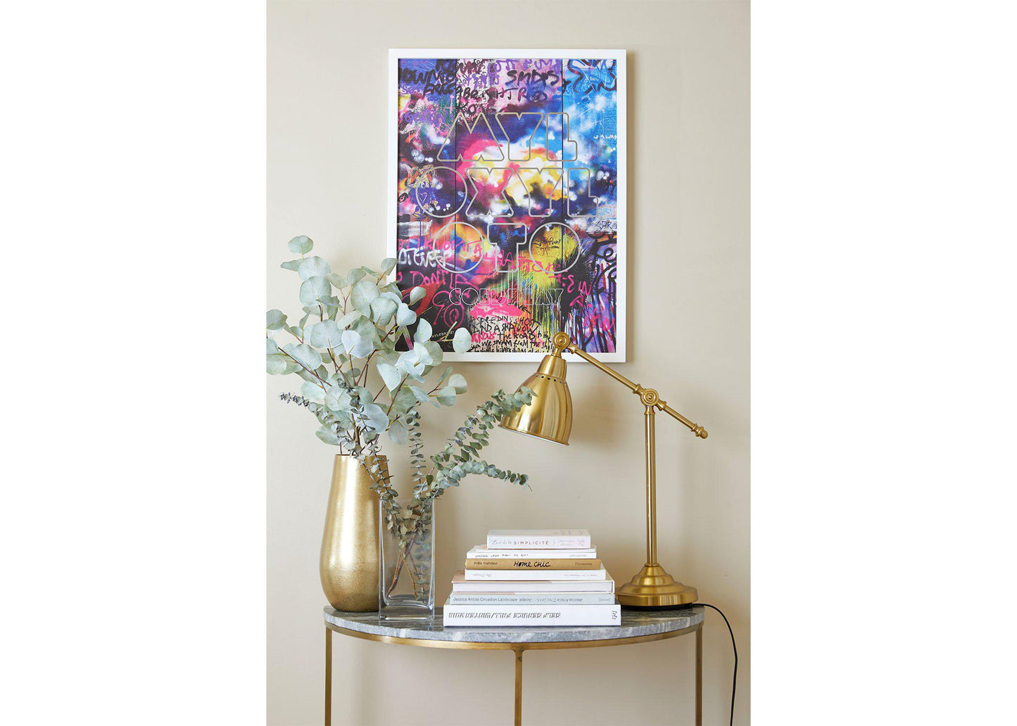 Image 4:
Mylo Xyloto Lithograph on a white frame, hung on a beige wall, above a small table shaped like a crescent moon, with a marble top and golden legs. The table has golden and clear vases with eucalyptus, books and a golden desk lamp. The poster's striking, expressive nature inspires rebellious energy and creativity