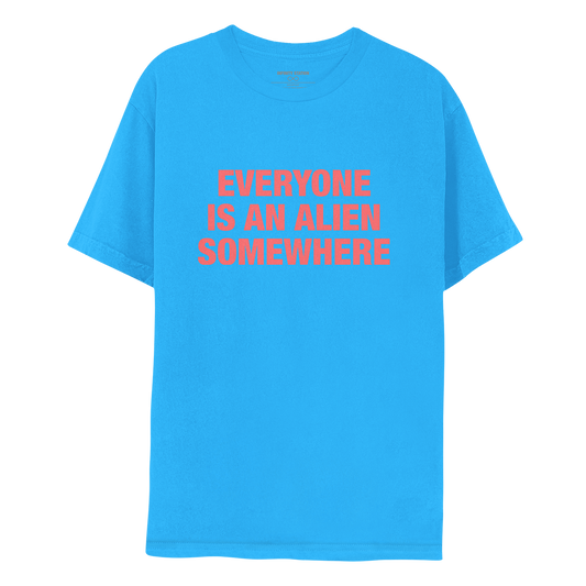 Front: This is Chris’s shirt. Fabric is a very vibrant blue. EVERYONE IS AN ALIEN SOMEWHERE is salmon pink. The text is large and bold, in 3 lines: EVERYONE, IS AN ALIEN, SOMEWHERE.  