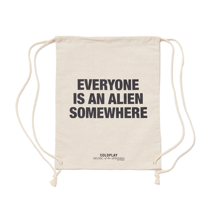 Natural cream-colored hemp bag, with EVERYONE IS AN ALIEN SOMEWHERE printed in large, bold black letters. MUSIC of the SPHERES printed below in black. The bag has drawstrings on each side, used to close it and carry it like a backpack.
