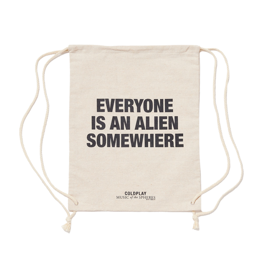 Natural cream-colored hemp bag, with EVERYONE IS AN ALIEN SOMEWHERE printed in large, bold black letters. MUSIC of the SPHERES printed below in black. The bag has drawstrings on each side, used to close it and carry it like a backpack.