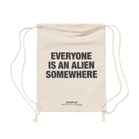 Natural cream-colored hemp bag, with EVERYONE IS AN ALIEN SOMEWHERE printed in large, bold black letters. MUSIC of the SPHERES printed below in black. The bag has drawstrings on each side, used to close it and carry it like a backpack. This photo shows a bit of slack in the fabric at the top which represents the opening.