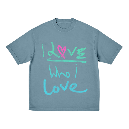 Front: The shirt is a soft green blue. The words I love Who I love are painted in a free, expressive brushstrokes fashion that suggests emotion and spontaneity. In the first I love, I&L are in light green. The O  is a pink fuchsia heart, drawn by hand. The rest of the first love word is light green. Who I love is light blue. The letters are creatively decorated, in an elegant style.